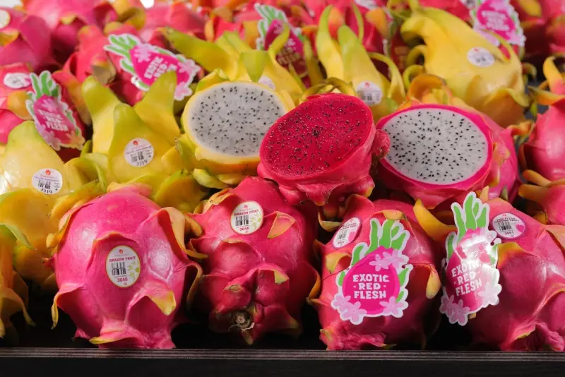 "Dragon fruit displayed, some halved, showing red and white flesh. Labels read ""Exotic Red Flesh"". "
