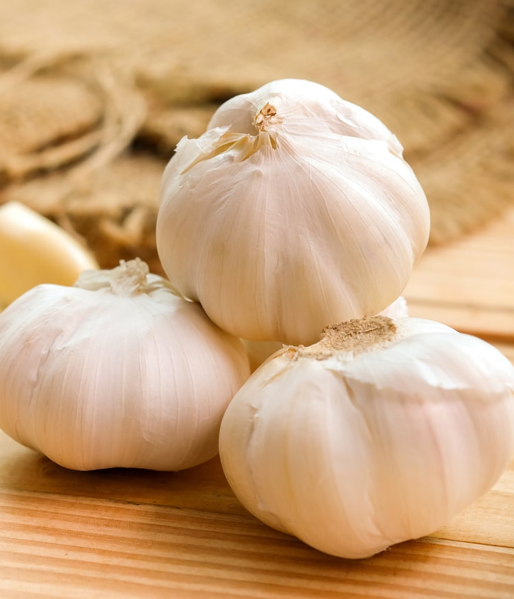 Garlic bulbs rest on wood.