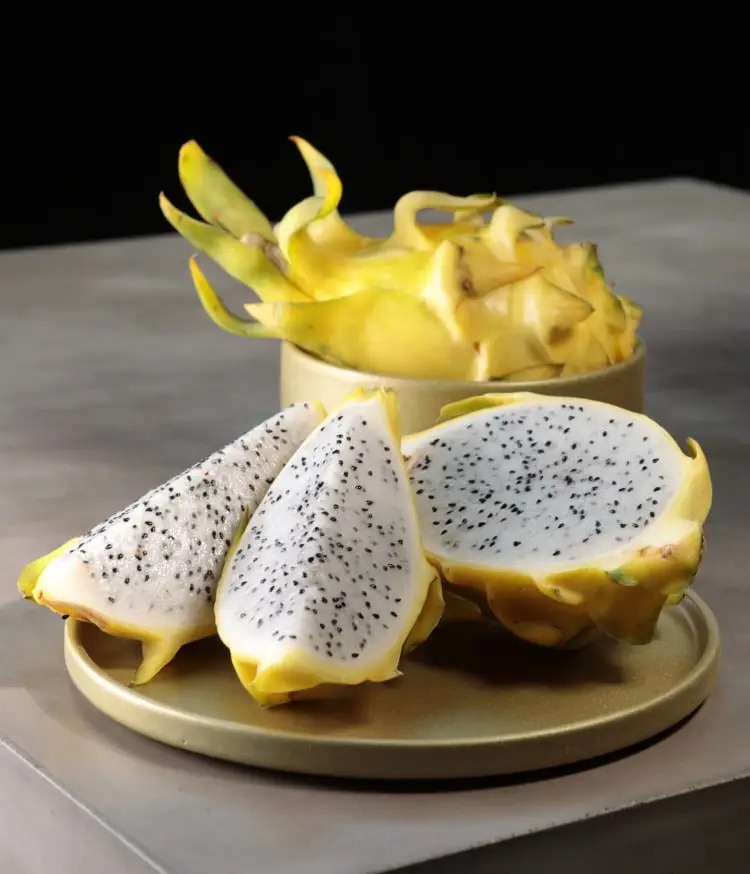 Yellow dragon fruit slices sit on a gold plate, next to a bowl of whole fruit.